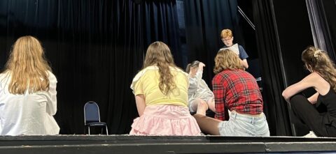 Young Company are onstage, watching two members rehearsing a script.